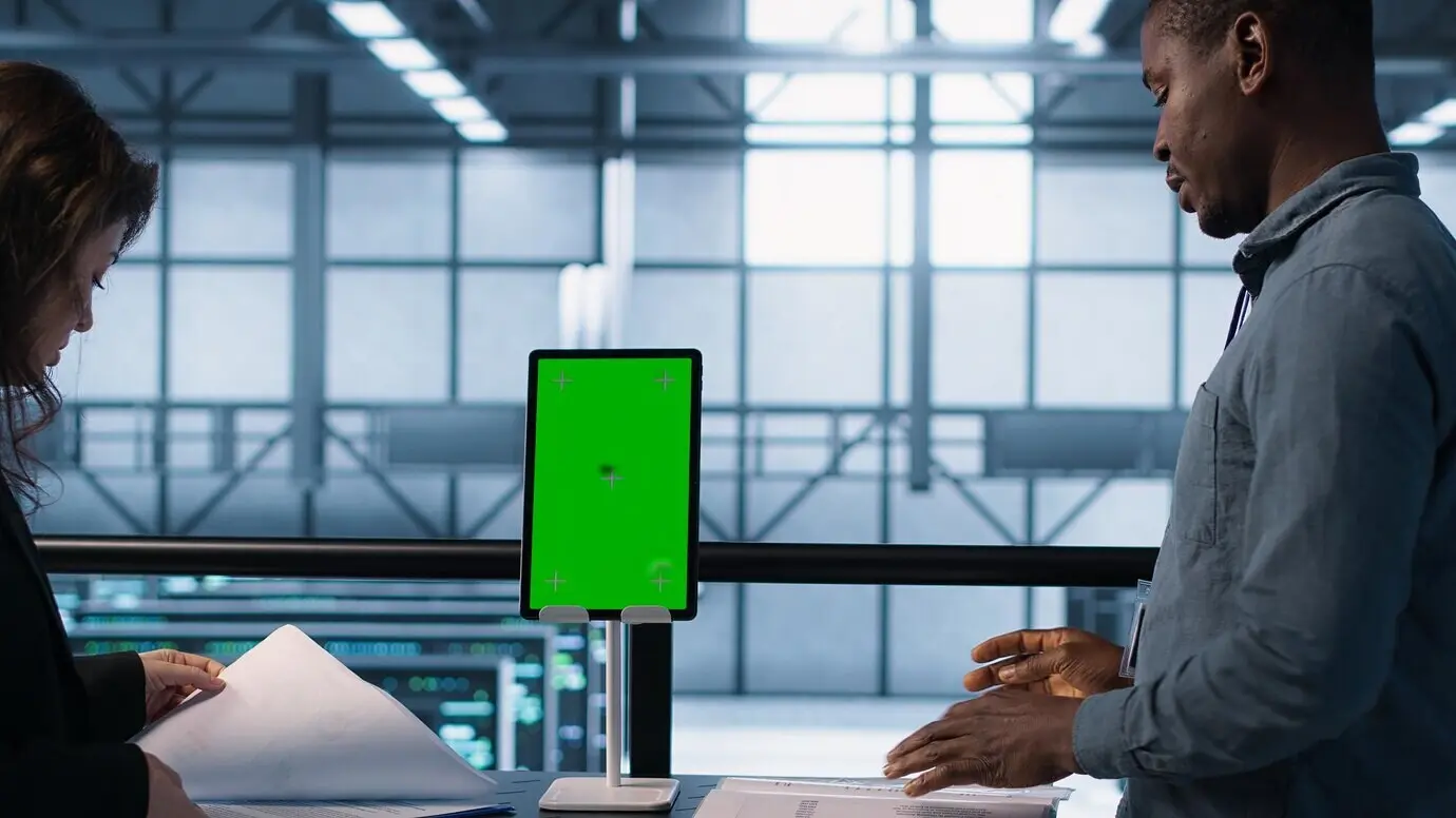 Инспектор проверяет документы в серверном узле и использует планшет с зелёным экраном.